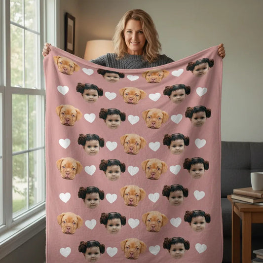 Person holding a pink blanket with dog and child faces and hearts pattern in a room.
