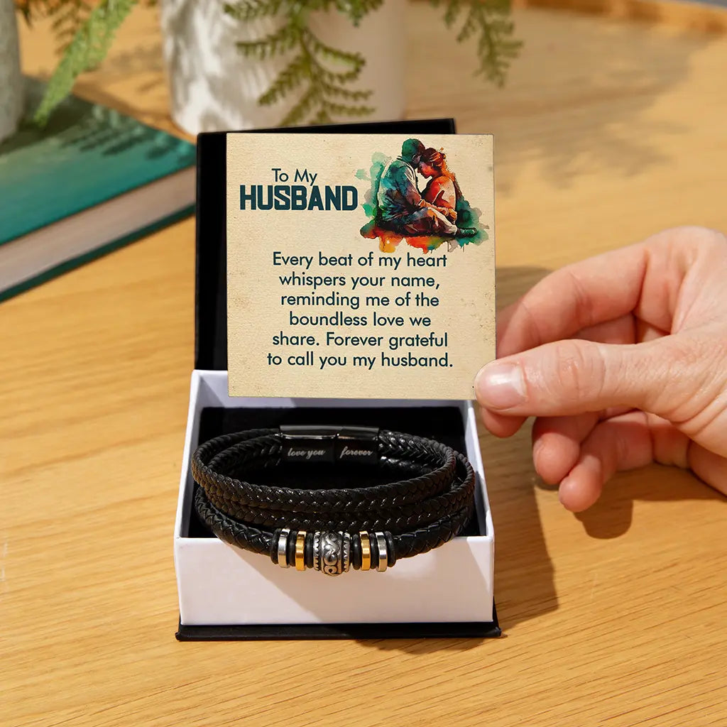 Black leather bracelets with gold accents in a box with a card for a husband on a wooden surface.