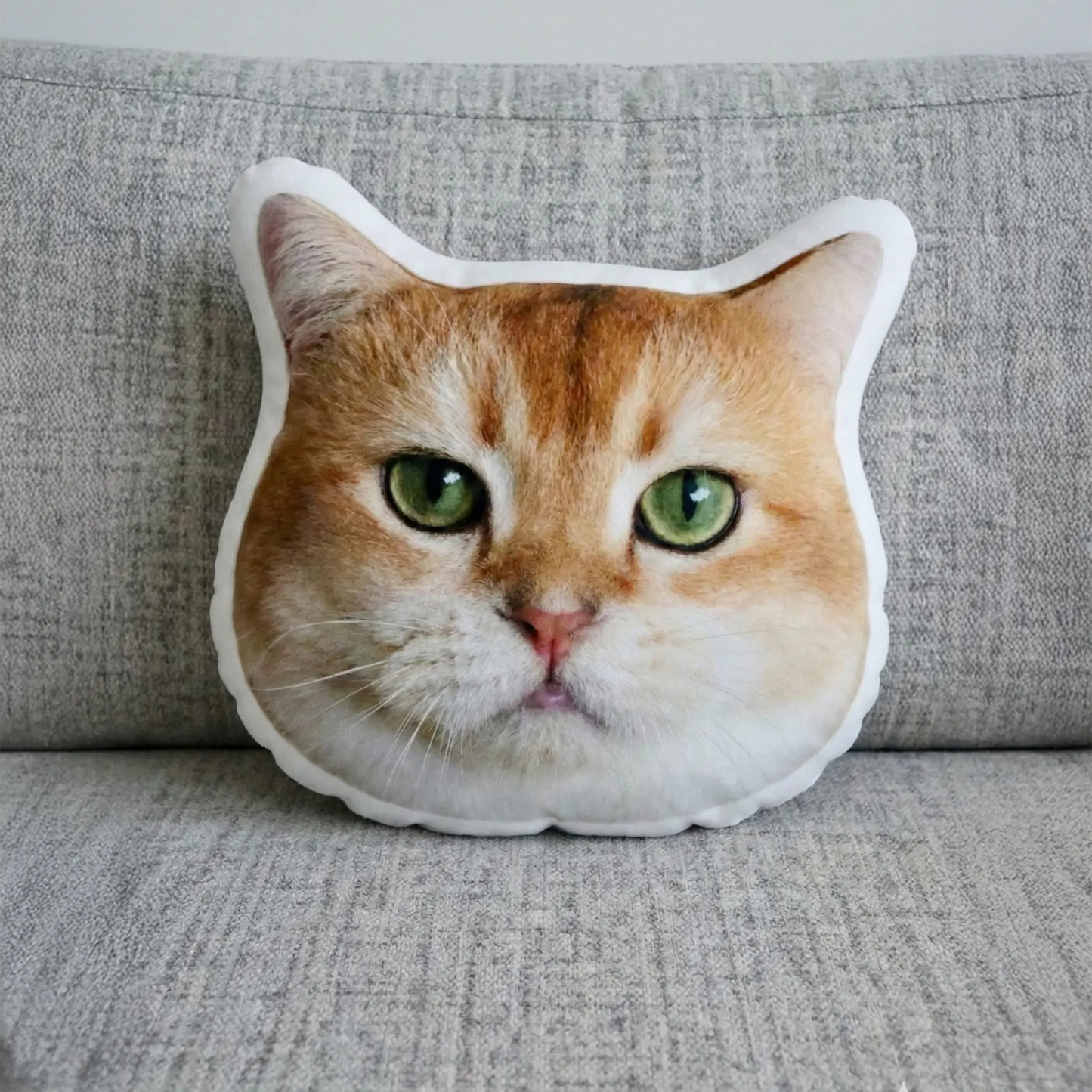 Cat-shaped pillow with a cat's face on a gray couch